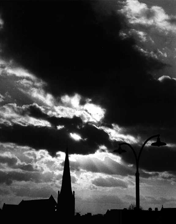 Black & white photograph. Church spire & stormy sky